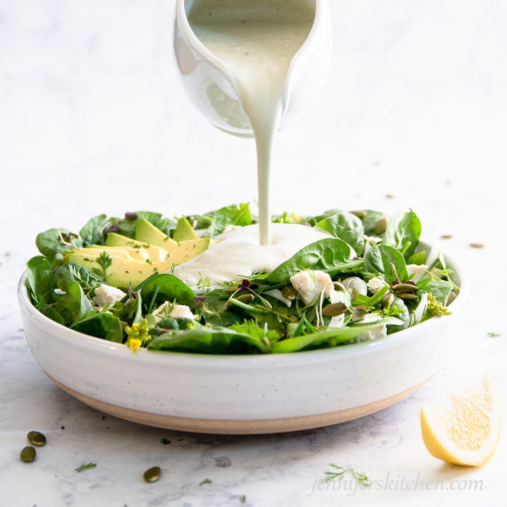 Pouring Creamy Pumpkin Seed Dressing over Spinach Avocado Salad.